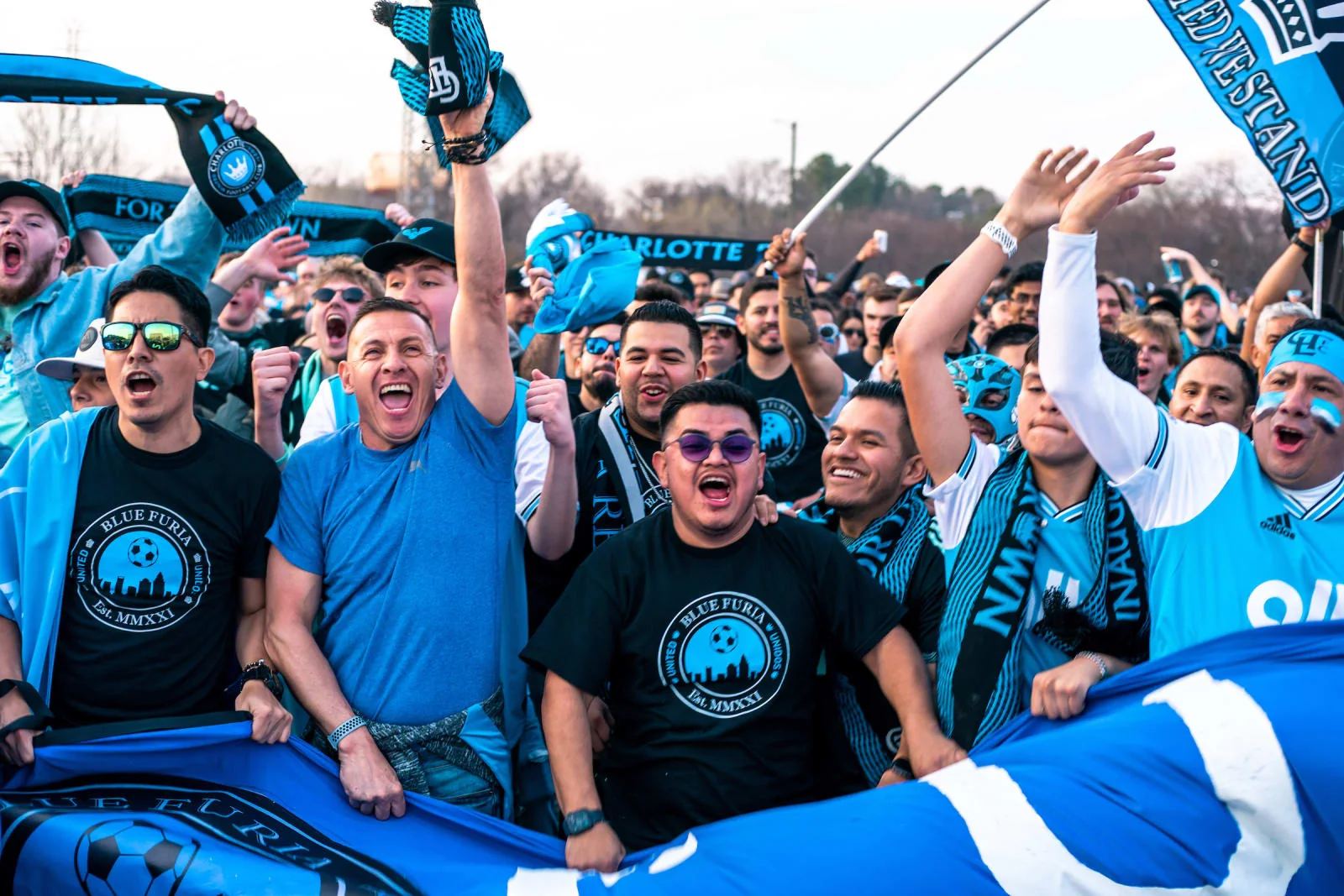 Charlotte FC supporters raising blue scarves and flags outside the stadium at the club's 2022 home opener