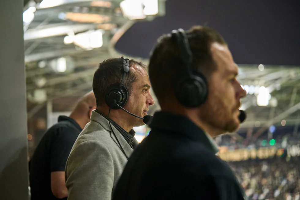 MLS broadcasters Max Bretos and Brian Dunseth wearing headsets at an LAFC match in 2023